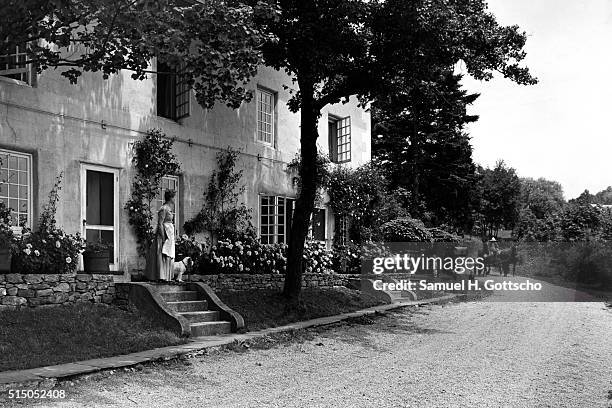 The front exterior of June and Joseph B. Platt's pre-Revolutionary New Jersey home with June in a long dress and apron standing with a small dog on...