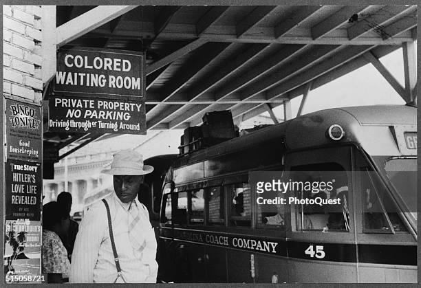 View of a passengers under a sign that reads 'Colored Waiting Room' at a bus station , Durham, North Carolina, 1940. Several buses, one from the...