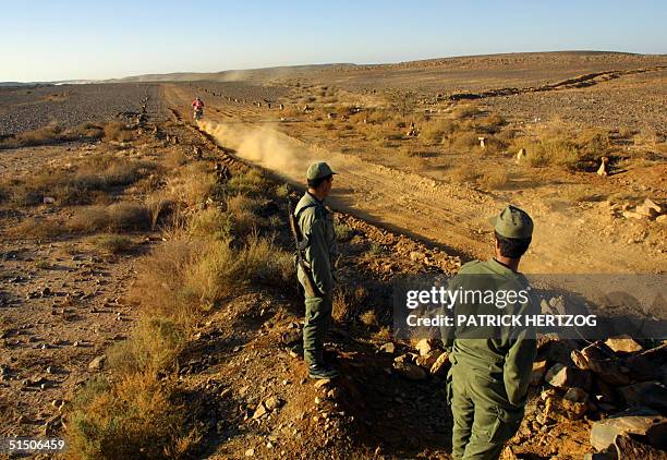 Moroccan soldiers watch a biker pass the wall of sand separating Morocco and Mauritania in the western Sahara on the eighth leg of the 23d Paris...