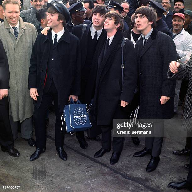 John Lennon, Paul McCartney, Ringo Starr, and George Harrison arrive at Idlewild Airport to the sight and sound of several hundred cheering fans who...