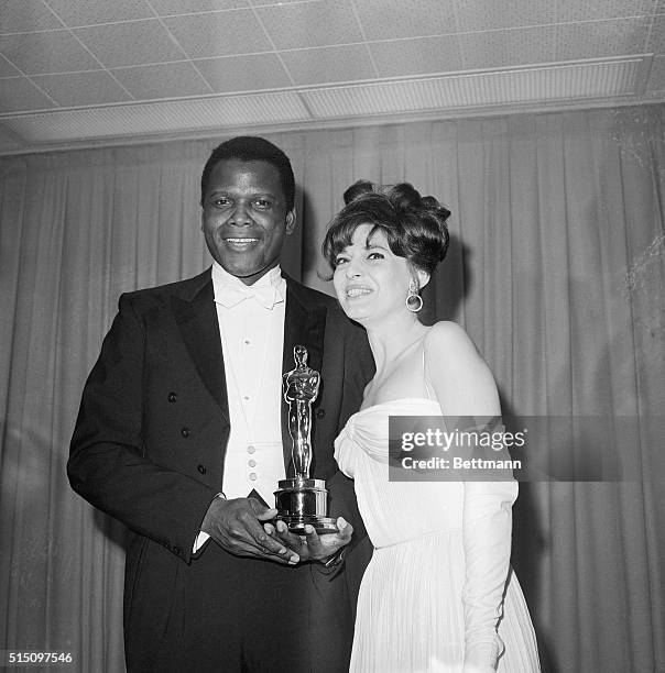 Sidney Poitier receives an Oscar presented by Anne Bancroft in Santa Monica, California, on April 13, 1964. He won Best Performance by an Actor for...