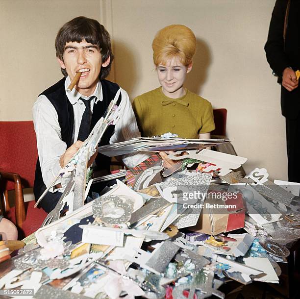 George Harrison smokes a cigar and holds birthday cards sent to him by fans. The young woman is from the Beatles' management company, NEMS, and was...
