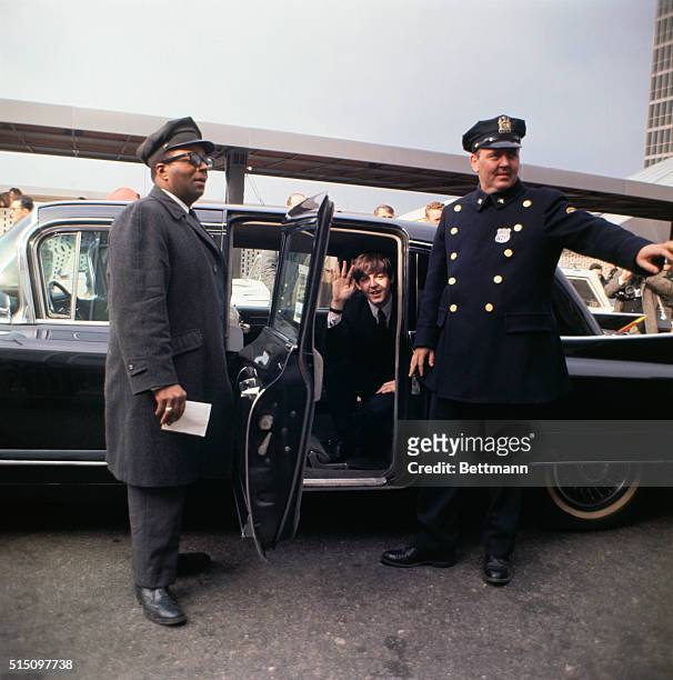 Flanked by a chauffeur and a police officer, British Rock musician Paul McCartney, of the group the Beatles, waves from the open door of a car at...