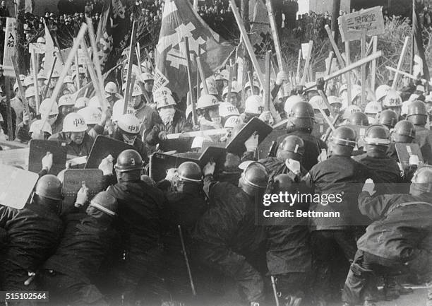 Phalanx of riot policemen marches behind shields at a mob of staff-swinging leftist students who are protected from expected blows to the head by...