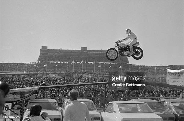 Motorcycle stunt man Evel Knievel sails over a line of 19 automobiles in a record breaking effort before the start of the Miller 500 stock car race...