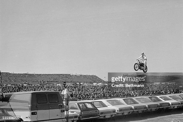 Motorcycle stunt man Evel Knievel sails over a line of 19 automobiles in a record breaking effort before the start of the Miller 500 stock car race...