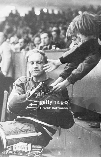 Bobby Hull of the Winnipeg Jets Hockey Team signs a autograph for a young fan while sitting out his penalty during the first period of a game against...