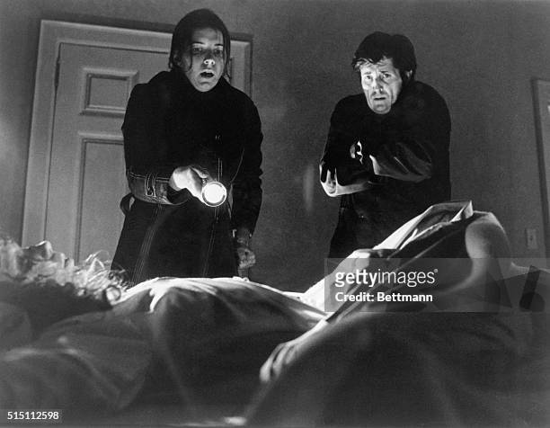 Kitty Winn holds a flashlight at Linda Blair, in bed, as Jason Miller watches in this scene from "The Exorcist."