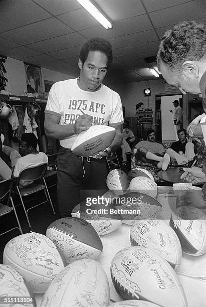 Buffalo Bills' O.J. Simpson signs footballs as Dolphins',Larry Csonka, relaxes prior to the AFC taking the field for practice.