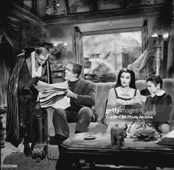 American actor and children's book author Fred Gwynne holds a newspaper and talks to Al Lewis while Canadian actor Yvonne de Carlo and child actor...