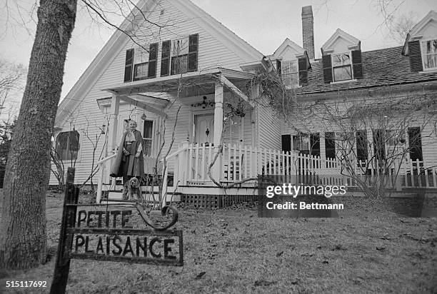 Marguerite Yourcenar, French novelist, essayist, and short story writer, stands on the porch of her home with her dog.