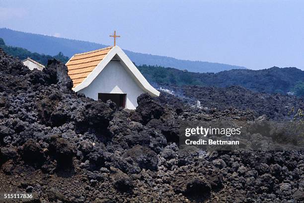 Villagers 8/8 pick over a lava flow on the slopes of the Mt. Etna volcano that surrounded the religious chapel of Sacro Cuore near Fornazzo, but...