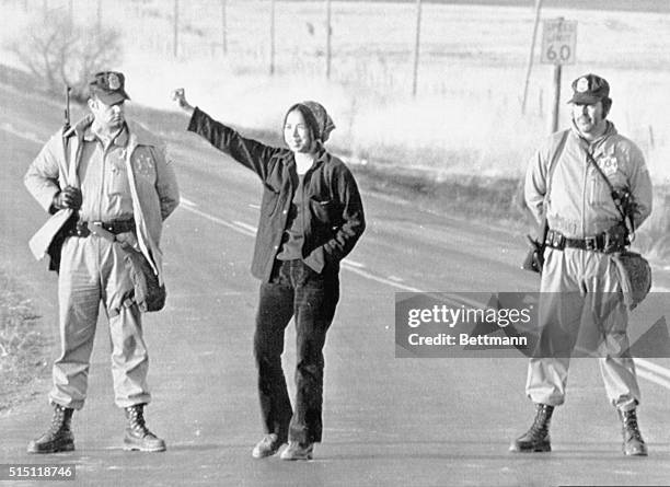 Marshals standing roadblock duty on the access road to Wounded Knee on March 1 watch as a Native American woman gives a clenched fist salute. On...