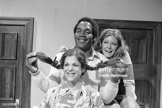 Football hero, O.J. Simpson, has a firm grasp on this situation as he checks out the length of TV comedienne, Gilda Radner's, pigtails as Jane Curtin...