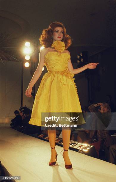 New York: Bill Blass presents this strapless yellow taffeta short dance hall dress, edged in taffeta pleats with a pleated taffeta rose at the neck...