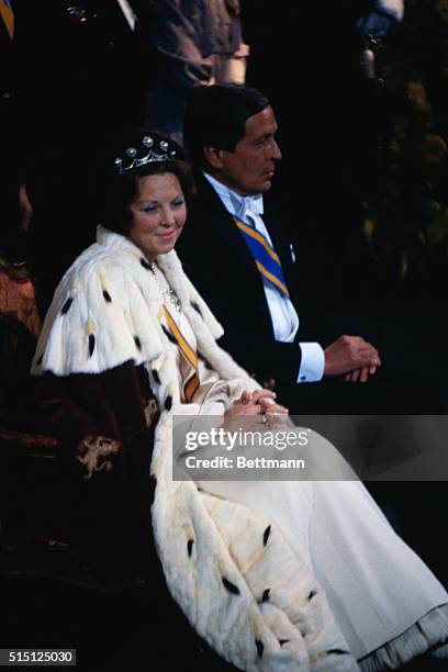 As Prince Claus looks on, Queen Beatrix of the Netherlands sits upon her throne during her investiture in the New Church in 1980.