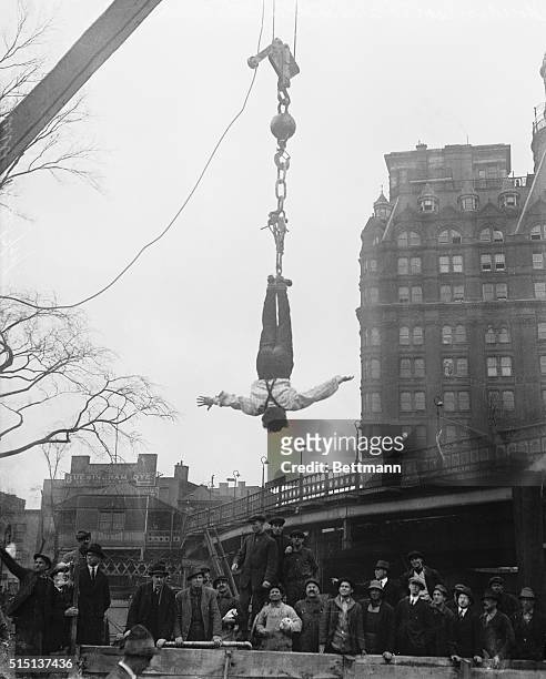 Harry Houdini hangs upside down from a crane after freeing himself from a straitjacket.