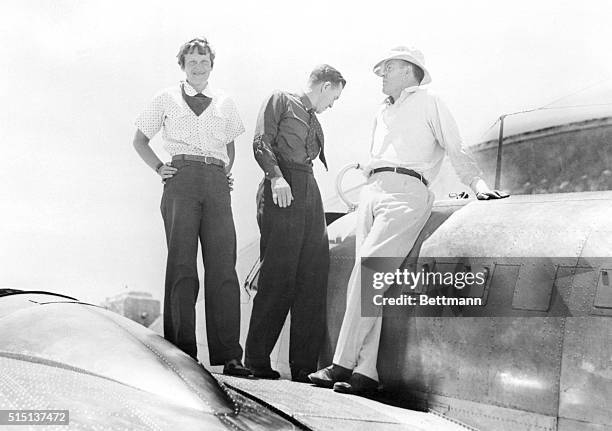 Amelia Earhart Putnam discusses radio trouble on the wings of her plane, a twin motored monoplane , with Captain Fred Noonan, her navigator, , and...