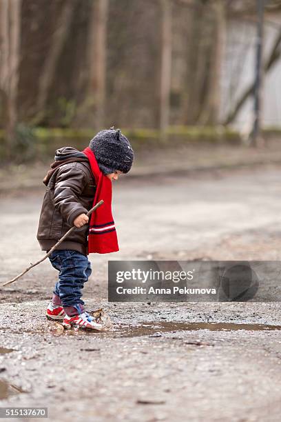 toddler boy with a stick playing ina puddle - eenjarig plantenkenmerk stockfoto's en -beelden
