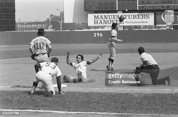 Under watchful eye of 3rd base coach Eddie Yost New York's Felix Millan slides safely into 3rd after tagging up at second on long fly by teammate...