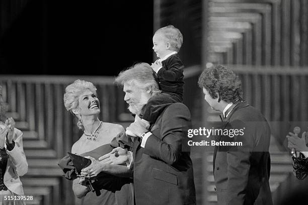 Los Angeles: Singer Kenny Rogers acknowledges the cheers of the audience as he holds his 13 month old son, Christopher Cody on his shoulders after...