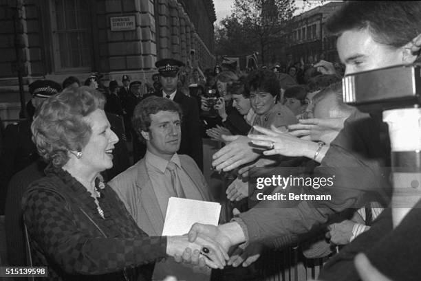 London, England- Jubilant crowds, at the barrier across Downing Street, are shown offering a cluster of hands for Britain's re-elected Prime...