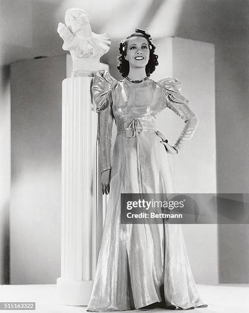 This regal empire gown of gold and orange lame, worn by Lily Pons, opera and film star, was designed by Edward Stevenson to enhance the dusky charms...