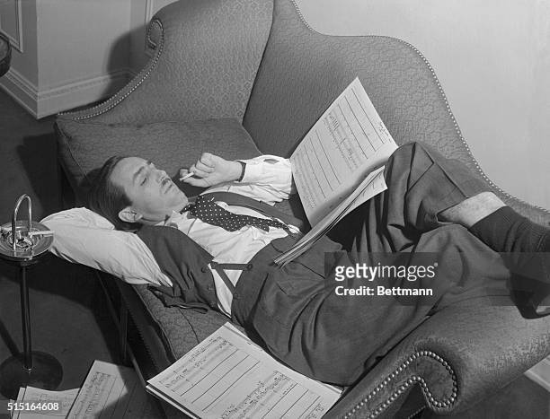 Walt Disney, famous animated cartoon producer, decorates the divan in his hotel suite as he checks over the musical scores that will eventually...