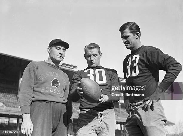 Coach Ray Flaherty, of the Washington Redskins, is shown giving instructions to his two passing aces, Frank Filchock and Sammy Baugh , as the squad...