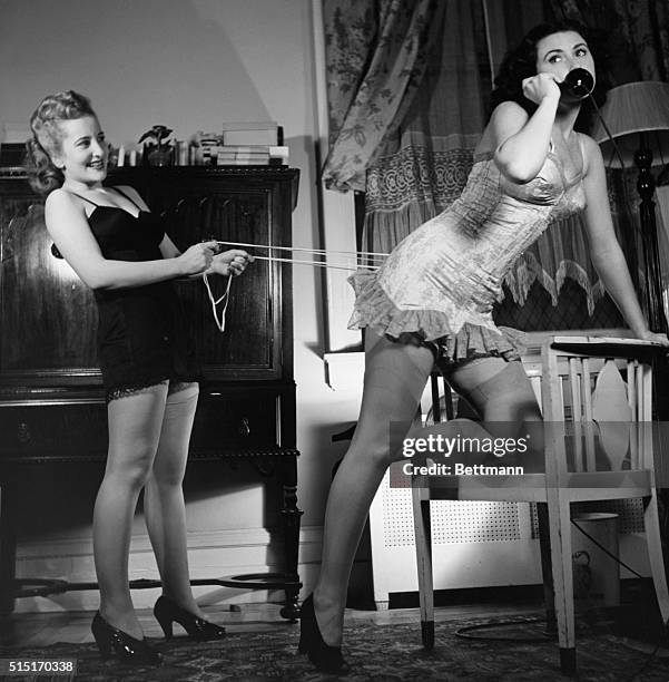 Photo shows a woman in her underwear on the telephone while another similarly clad woman behind her tightens her corset. Undated photograph.