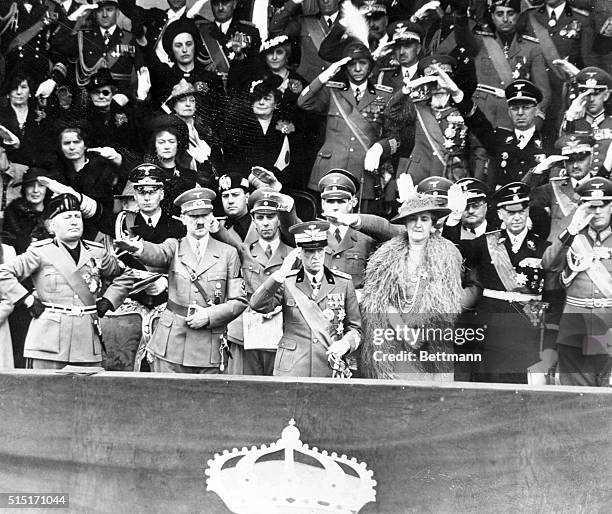 Arms akimbo, premier Benito Mussolini views a parade of Italian might with his "pal" Adolf Hitler, King Victor Emmanuel, and Queen Elena, in Rome,...