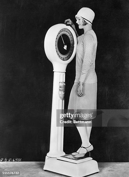 Flapper weighing herself on scale. Photograph, ca. 1920.