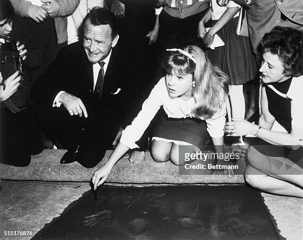 British teenage actress Hayley Mills plants her hands in the forecourt of Grauman's Chinese Theatre, her parents, British actor John Mills and writer...