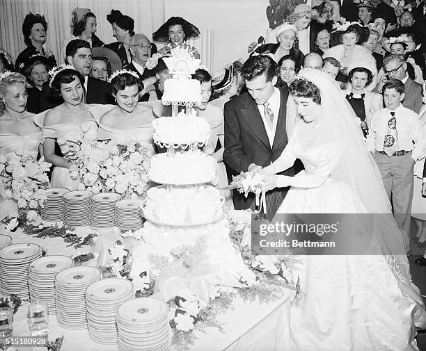 Beverly Hills, CA: Conrad Nicholson Hilton, Jr., heir to a hotel fortune, and his bride, actress Elizabeth Taylor, cut their huge wedding cake at a...