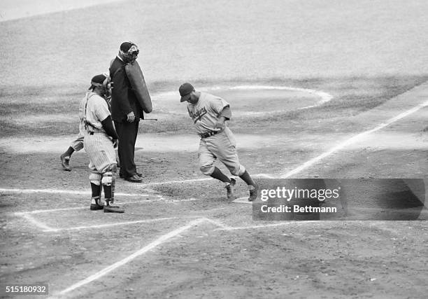 New York, NY: While a downcast Yogi Berra, Yankee catcher, and plate umpire Honochick look on, Roy Campanella of the Dodgers trots across the plate...