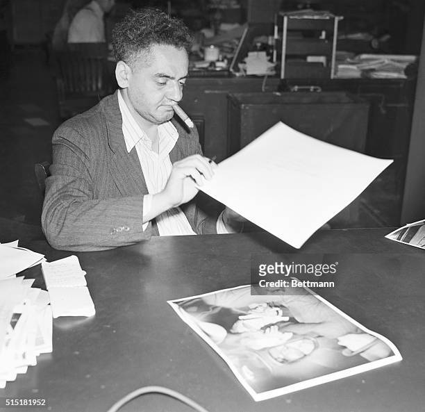Portrait of well-known New York freelance photographer Arthur "Weegee" Fellig, seated at his desk examining photos, with a cigar in his mouth. Photo...