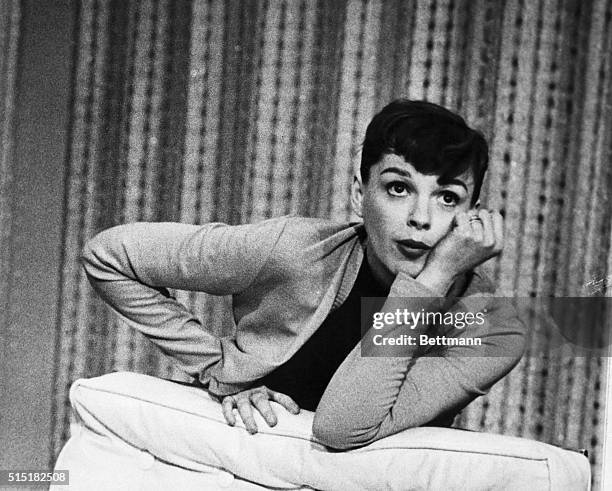 Judy Garland in a theater production. She wears a cardigan and has her hair pulled back. She leans on a cushion, with one hand supporting her face...