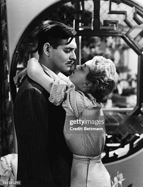Movie still of Clark Gable being hugged by a blonde actress as they stand before a picture window. He has a small moustache and looks upset with the...
