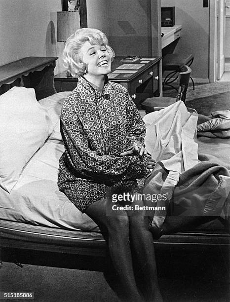 Doris Day in a scene from the 1961 Universal Pictures production "Lover Come Back." In this image, Day is shown seated on the edge of a bed, smiling.