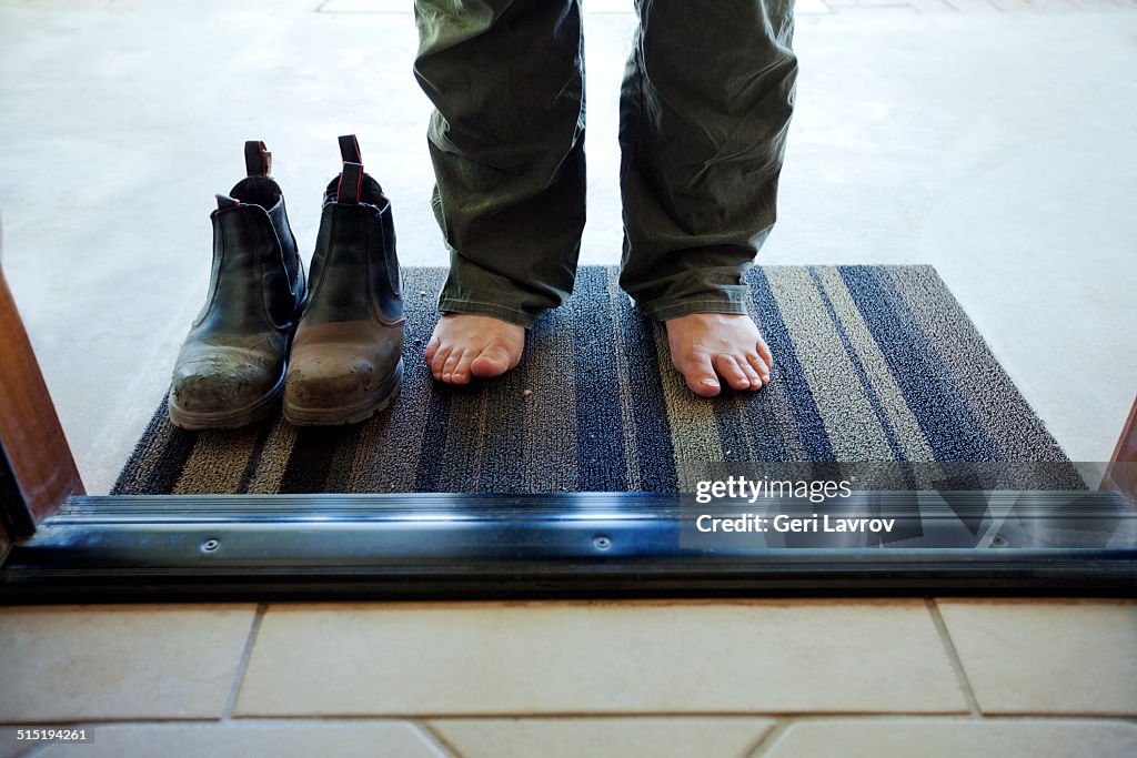 Barefoot man and his dirty boots at a front door