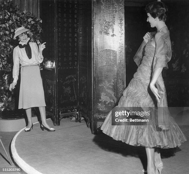 Coco Chanel admires a flounced brown chiffon evening dress from her new collection.