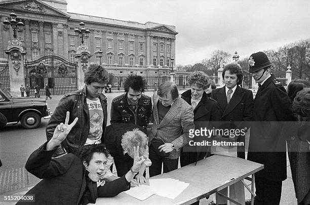 The punk rock group, The Sex Pistols, are about to be moved by a policeman as they sign a copy of their new recording contract with A & M Records...