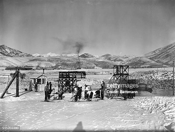 Sun Valley, ID- Photo shows a class of skiers attaching skis after arriving at Dollar Mountain, Sun Valley in the background. The machinery in the...