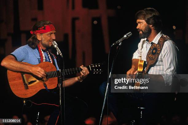 Country Western singer Glen Campbell and Willie Nelson playing guitar and singing onstage during a concert.