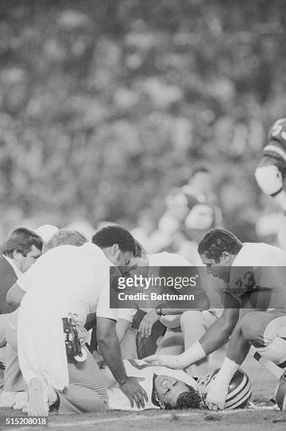 Athletic trainers and an unidentified Redskins player surround Redskins quarterback Joe Theismann on the field at RFK Stadium after Theismann broke...
