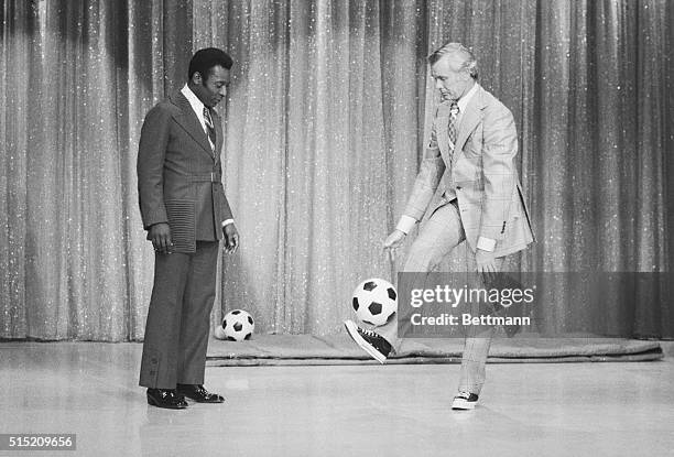 Wearing sneakers, TV star Johnny Carson gets some pointers on the art of kicking a soccer ball from Edson Arantes do Nascimento, better known as...