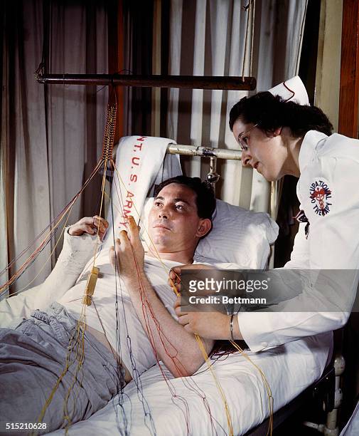 Wounded convalescing at Walter Reed Hospital. A nurse is by his side as he weaves a craft in bed.