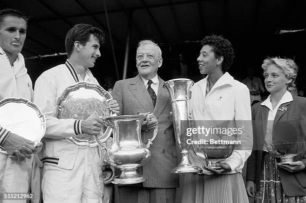 Forest Hills, NY- U.S. Secretary of State John Foster Dulles stands between winners of the national tennis singles match. Laden with trophies are...