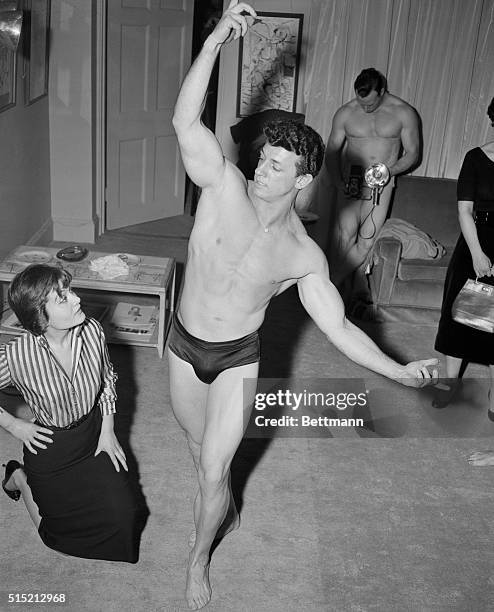 New York, NY:Miss Novella Parigini is shown looking over the winner of a "Typical American Male" contest,Don Armand,while in the background a...