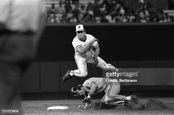Baltimore Orioles' shortstop Cal Ripken, Jr., hurdles Cleveland Indians' Andy Allanson as he throws to first to complete a double play on a ball hit...